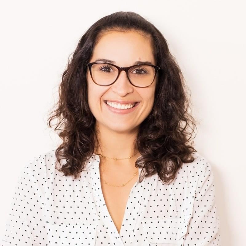 Headshot of a smiling Brazilian woman with medium length brown hair and glasses.