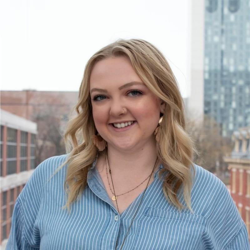 Headshot of a smiling white woman with medium length blond hair, wearing a pinstriped collard shirt.