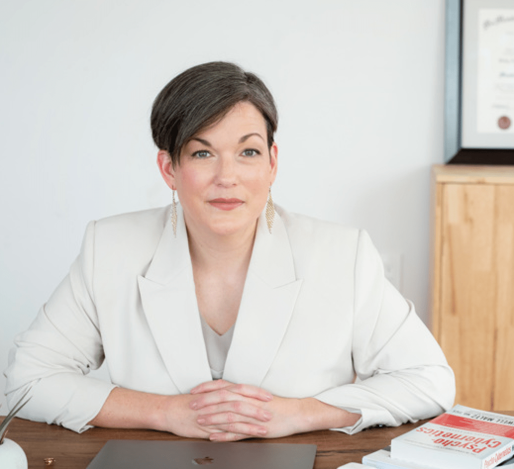 White woman with short brown hair wearing a white blazer smiling slightly.